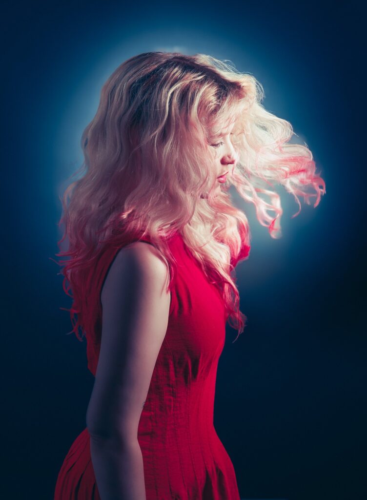 Fine art portrait of a woman in a red dress, wavy blonde hair in motion, glowing blue halo light, Brussels studio