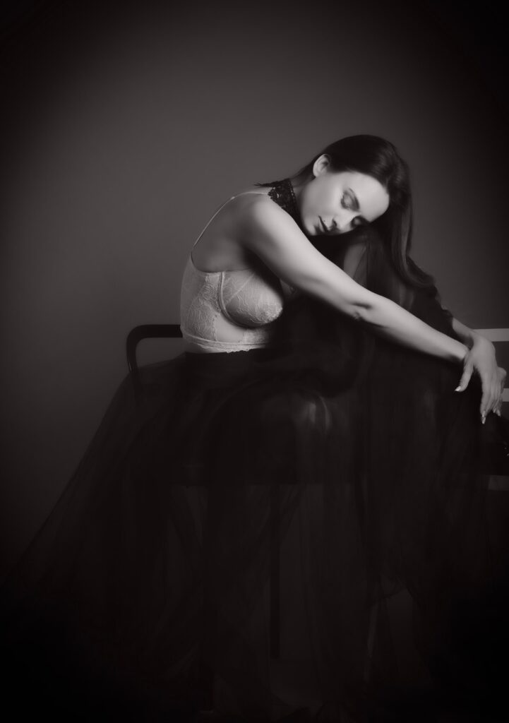 Black and white boudoir portrait of a woman in lace and tulle, resting her head on her shoulder in soft studio light