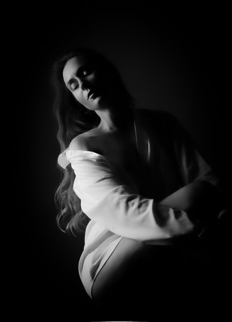 Black and white fine art boudoir portrait of a woman in an off-shoulder white shirt, low-key light, Brussels studio