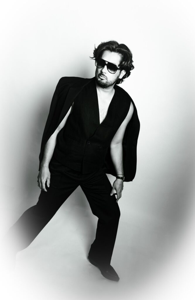 Black and white portrait of a man in sunglasses with a suit jacket draped over his shoulders like a cape