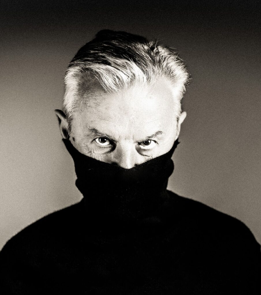 Black and white fine art portrait of a silver-haired man hiding his face in a black turtleneck, intense gaze, Brussels