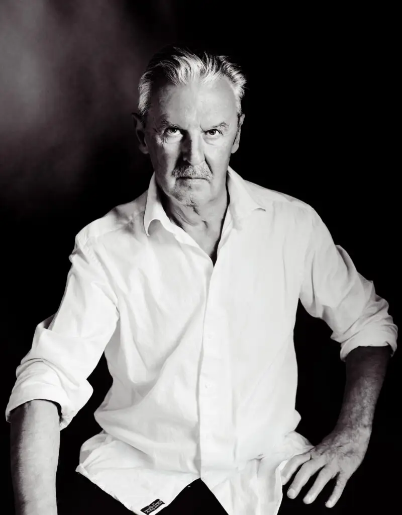 Black and white studio portrait of a mature man with a moustache in a white shirt, serious expression, Brussels
