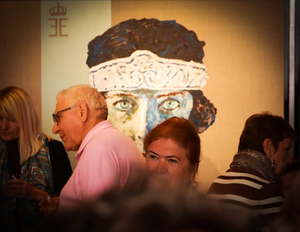 Candid moment of guests mingling in front of a painted portrait whose eyes echo a guest's gaze, warm evening light