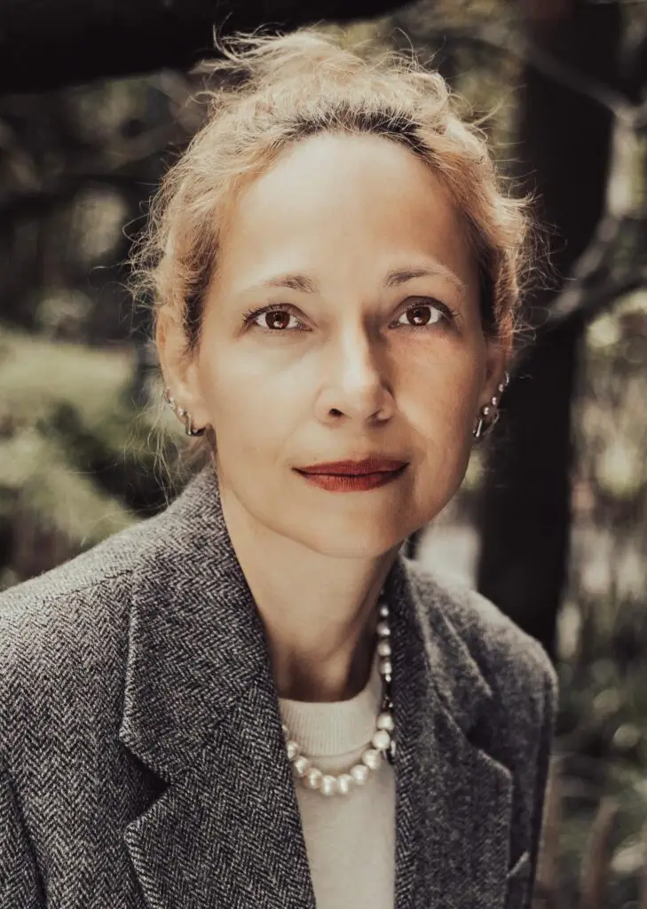 Elegant editorial portrait of a woman with a pearl necklace and herringbone blazer, warm muted tones, outdoors
