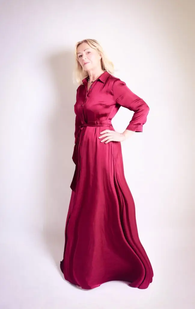 Full-length studio portrait of a confident woman in a flowing burgundy satin shirt dress, hand on hip