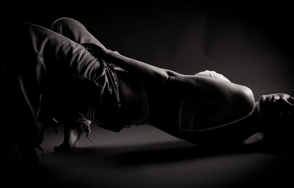 Low-key boudoir silhouette of a woman in jeans and lace reclining on the floor, light tracing the curve of her arm