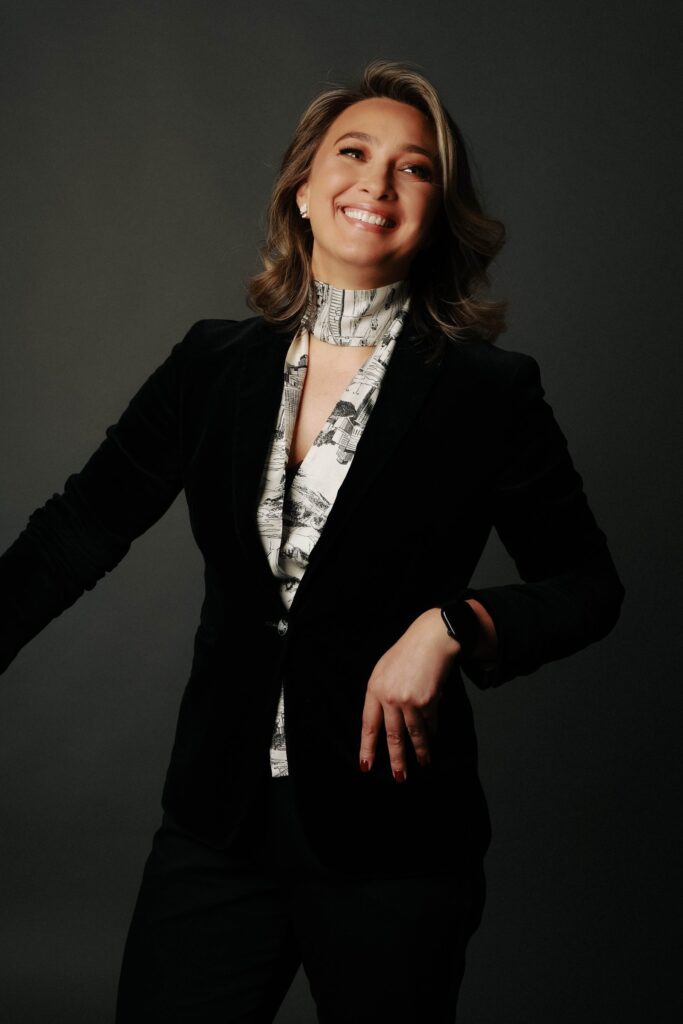 Black and white studio portrait of a woman in bold geometric glasses, velvet blazer and printed silk scarf, Brussels