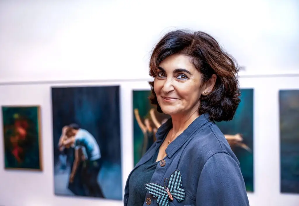 Portrait of a smiling woman with a beaded butterfly brooch in an art gallery, paintings softly blurred behind her, Brussels