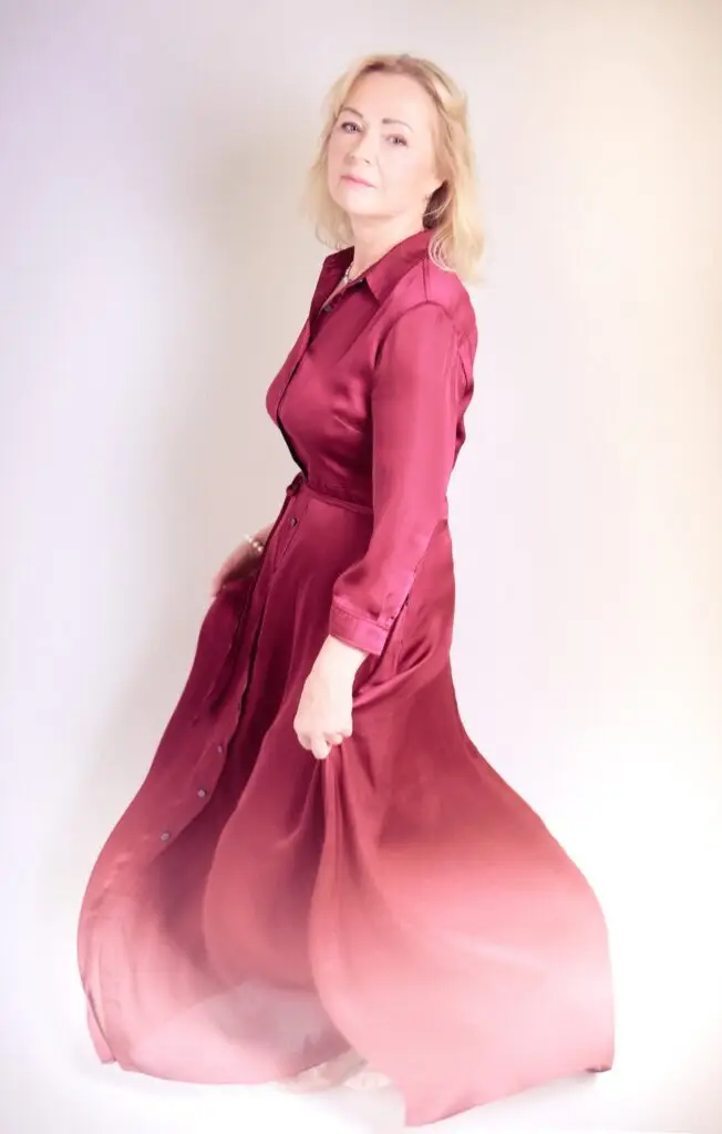 Dreamy portrait of a woman in a burgundy dress caught in motion, the satin fading into soft pink light