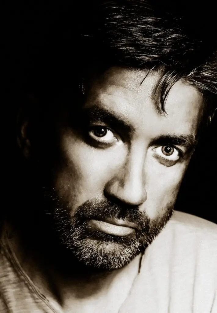 Dramatic sepia close-up portrait of a bearded man with an intense gaze, low-key studio light, Brussels