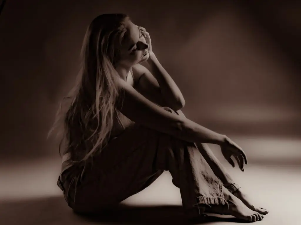 Soft sepia boudoir portrait of a woman with very long hair seated on the floor, hand to her face, eyes closed