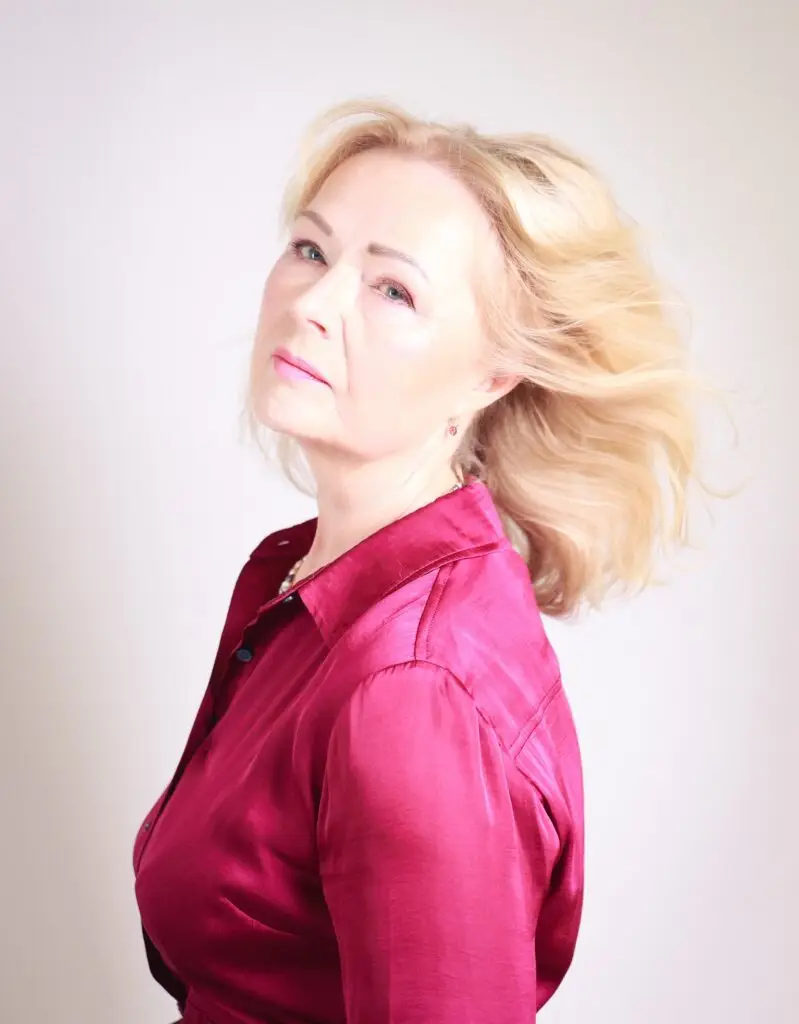 Studio portrait of an elegant mature woman in a magenta satin shirt, blonde hair swept by the wind